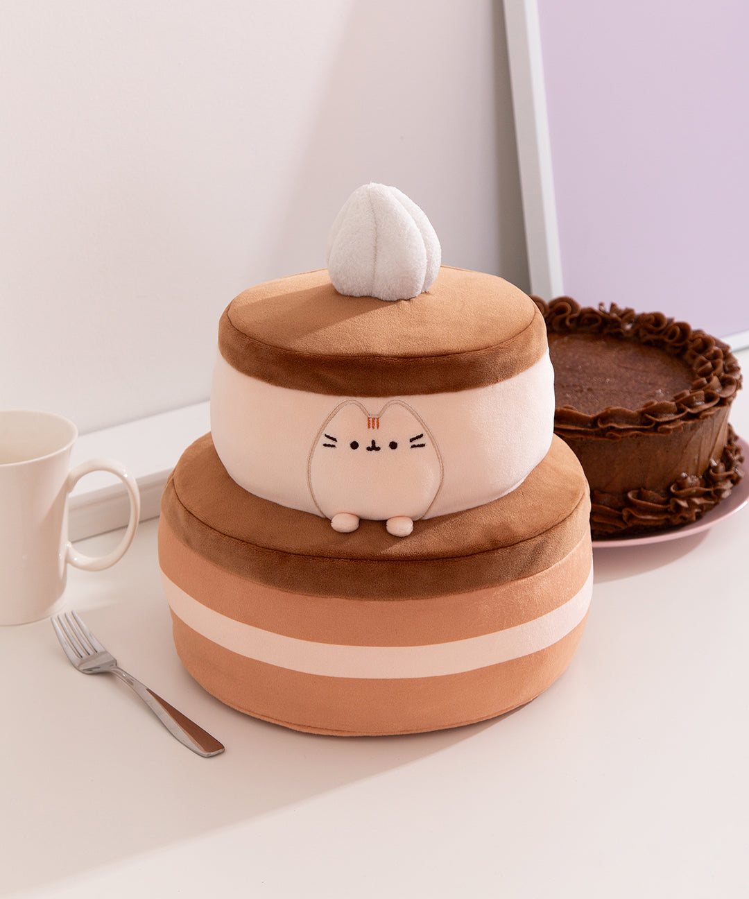 Front view of the Pusheen Sweets Chocolate Cake Squisheen Plush. The light brown Pusheen plush sits within the layers of the cake that's topped with whipped cream.