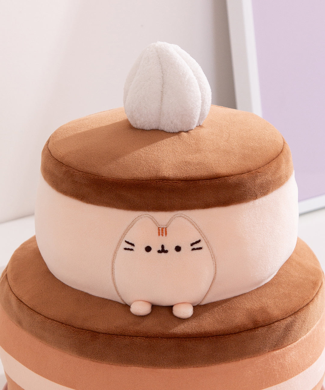 Close-up of the Pusheen figure within the plush cake layers. Pusheen the Cat's two front paws sit outside the top cake layer resting on the bottom layer.