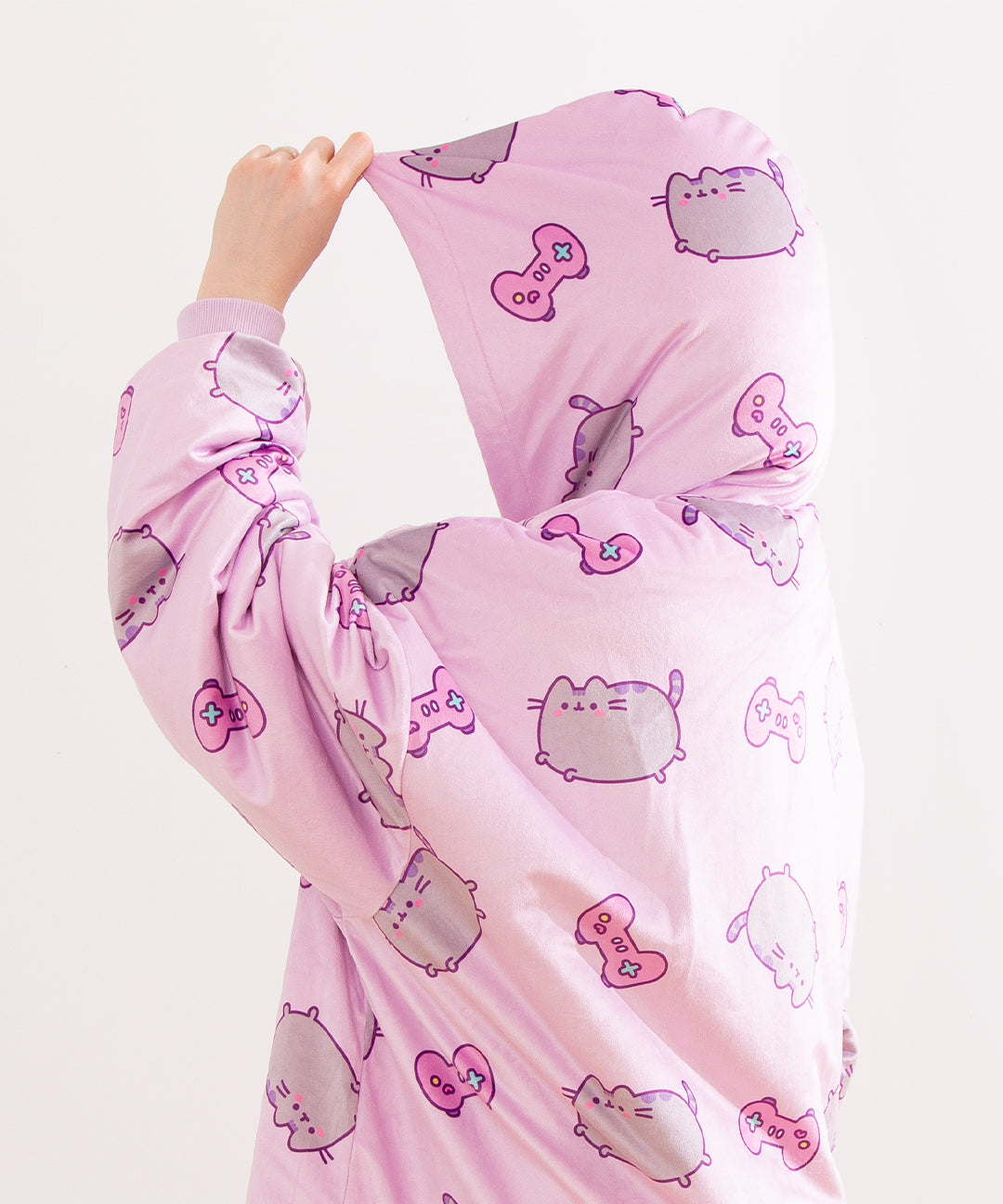 Model stands to the side while wearing the Gamer Pusheen Wearable Blanket Hoodie with the purple hood over their head. The print all over continues from the body onto the hood. The oversized hoodie fits most.  