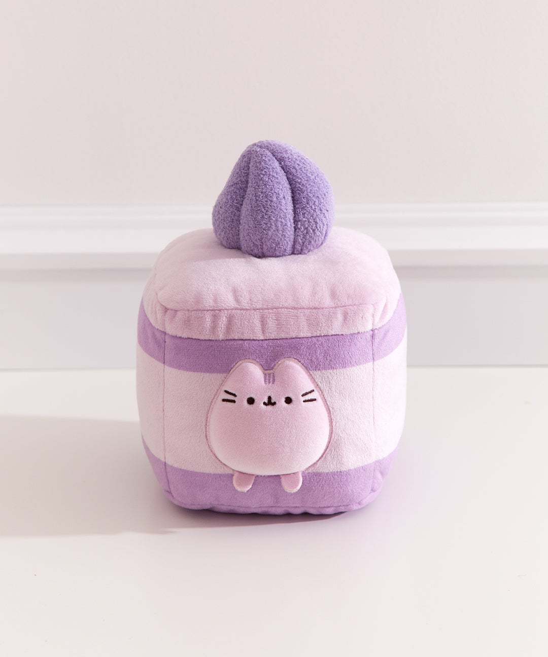 Pusheen Sweets Lavender Sponge Cake Squisheen Plush is a layered lavender sponge cake with alternating medium purple cake, light purple cream, and light purple icing. The cake is topped with a dark purple textured whipped cream plush dollop.