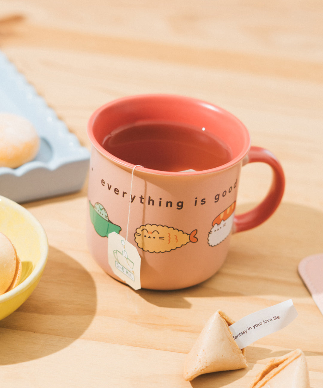 Pusheen Bento Mug filled with tea and a tea bag hanging from the side to show the function of the mug and that the inside mug color is coral-colored to match the handle color.