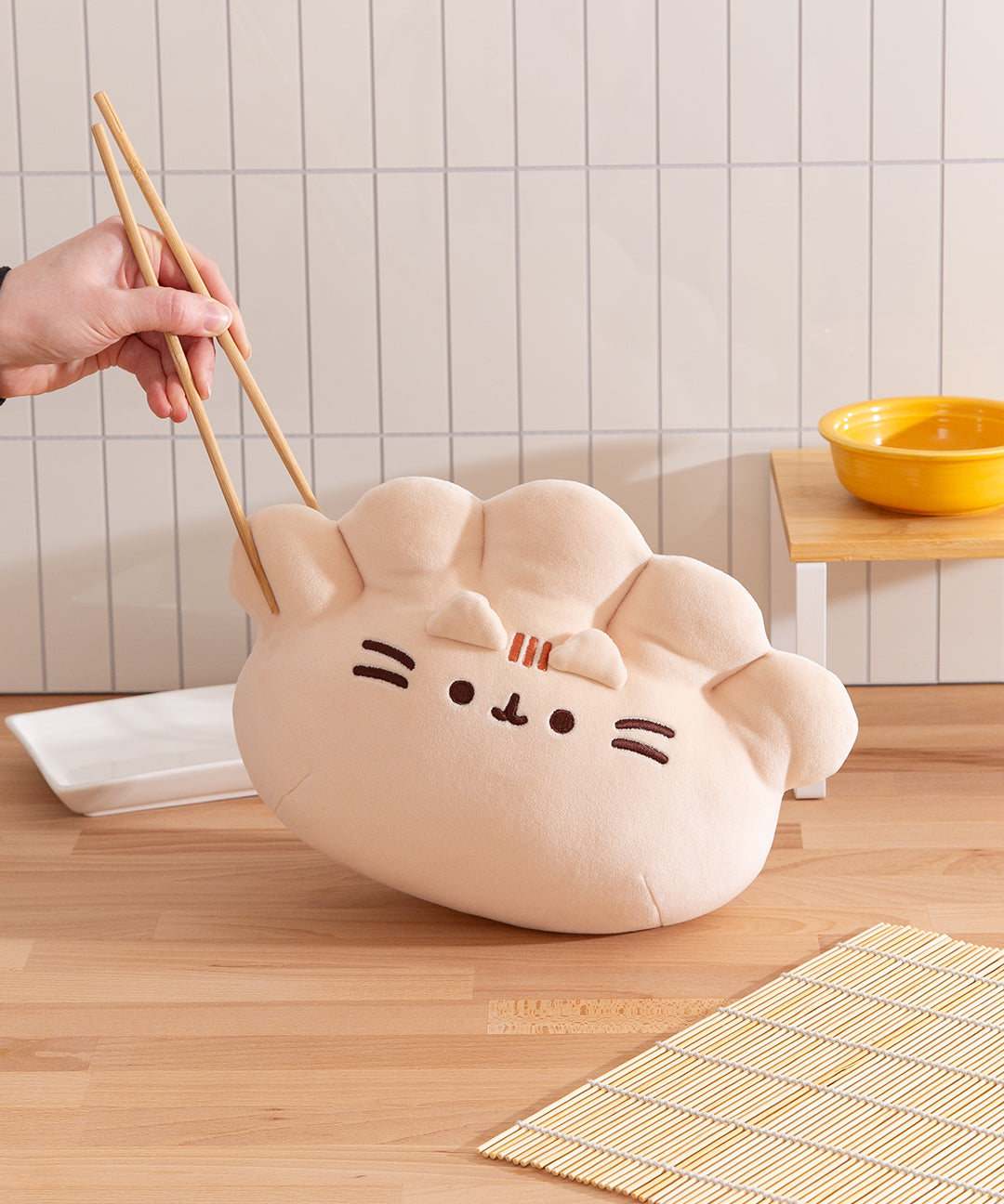 Model holds edge of the dumpling plush with chopsticks to show the squishy feel of the plush.