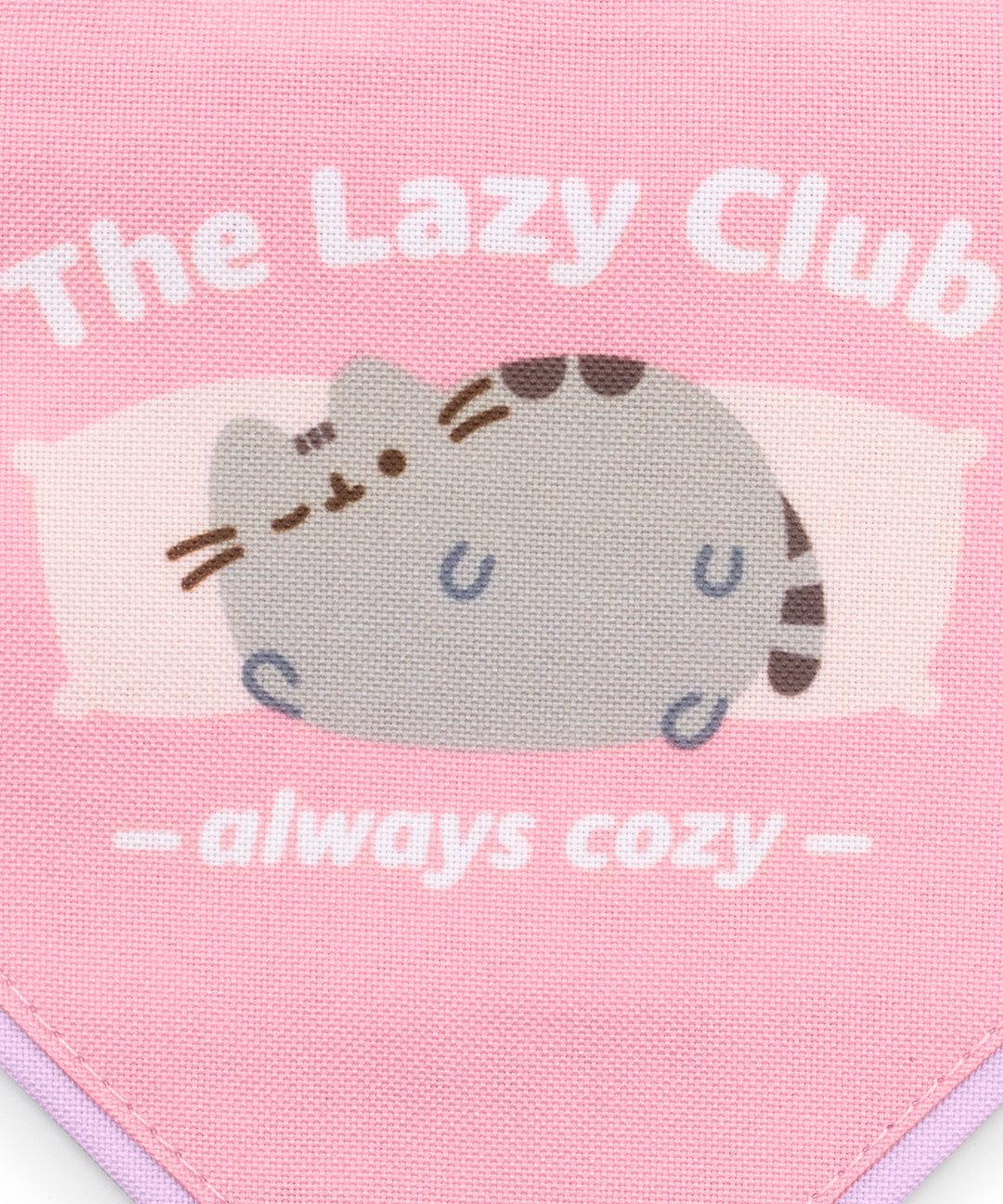 Close-up of the Bandana design that shows Pusheen lounging on light pink pillowsand winking in front of a pink background. Above and below the graphic are the phrases "The Lazy Club" and "always cozy" in white text.