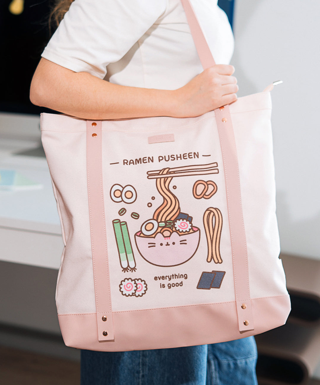 Model carries the Pusheen Ramen Deluxe Tote on their shoulder to show the size and scale of the cotton tote bag.