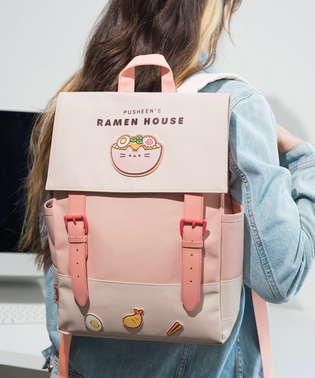Model wears the Pusheen Ramen House Backpack to show the size and scale of the light pink backpack. The backpack has a flap closure and features ramen-themed silicone patches.
