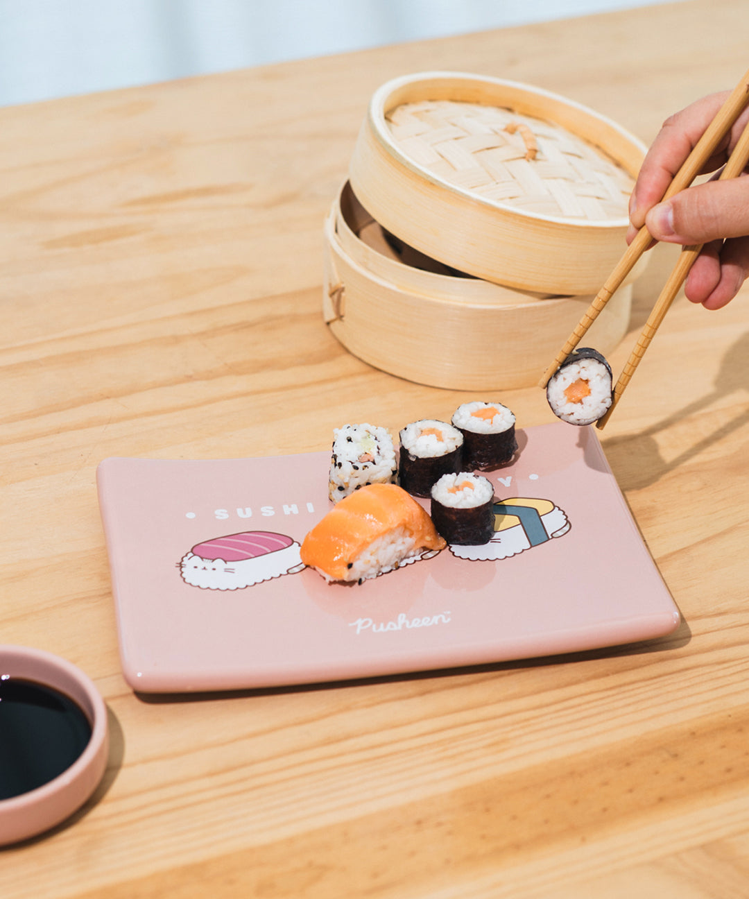 Model picking up a sushi roll with the included chopsticks from the tray included in the Sushi Set. The soy sauce dish sits off to the side.