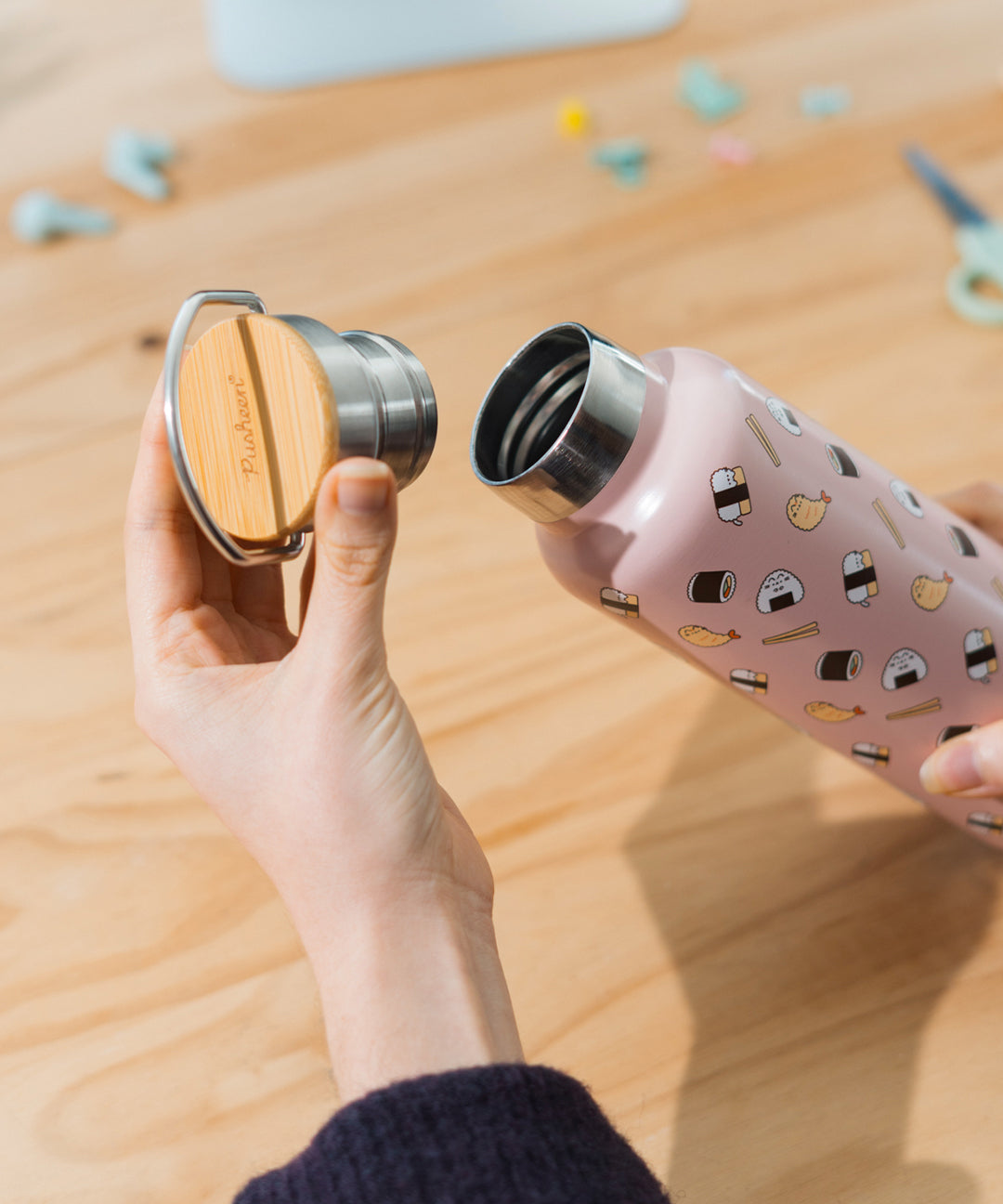 Model holding the cap of the stainless steel water bottle. The top of the cap is wooden with a metal handle and the interior is stainless steel.