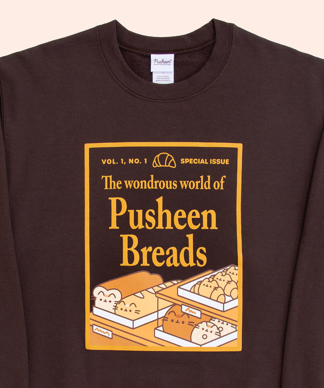 A close-up view of the screen-printed graphic of the Pusheen Breads Unisex Sweatshirt. The golden, magazine-style graphic features Pusheen Breads in bakery case surrounded by a golden, rectangle border.  