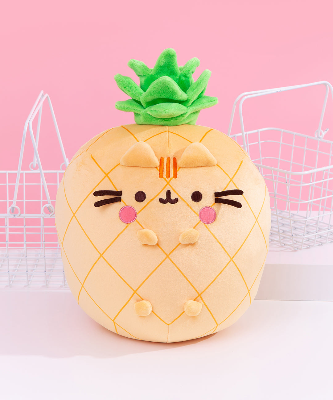 Front view of the Pusheen Fruits Scented Pineapple Squisheen Plush. Pusheen the Cat takes the form of a yellow pineapple. The yellow body of the plush has darker yellow grid lines that mimic the features of a pineapple. On the front of the plush are 3D versions of Pusheen’s ears and four paws. The yellow plush is topped with a vibrant green pineapple crown of leaves.  