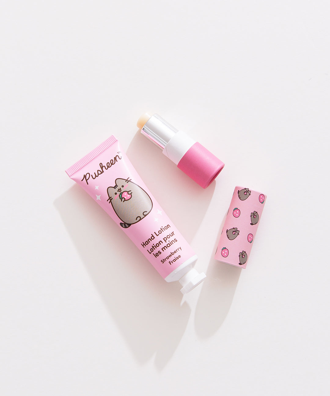 Lip balm and lotion lie on a white desktop. The Pusheen-themed set has a strawberry scented lotion. 