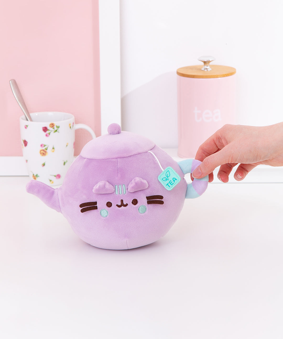 Model holds handle of the Teapot Plush. The handle is a striped light blue and lilac purple ring.