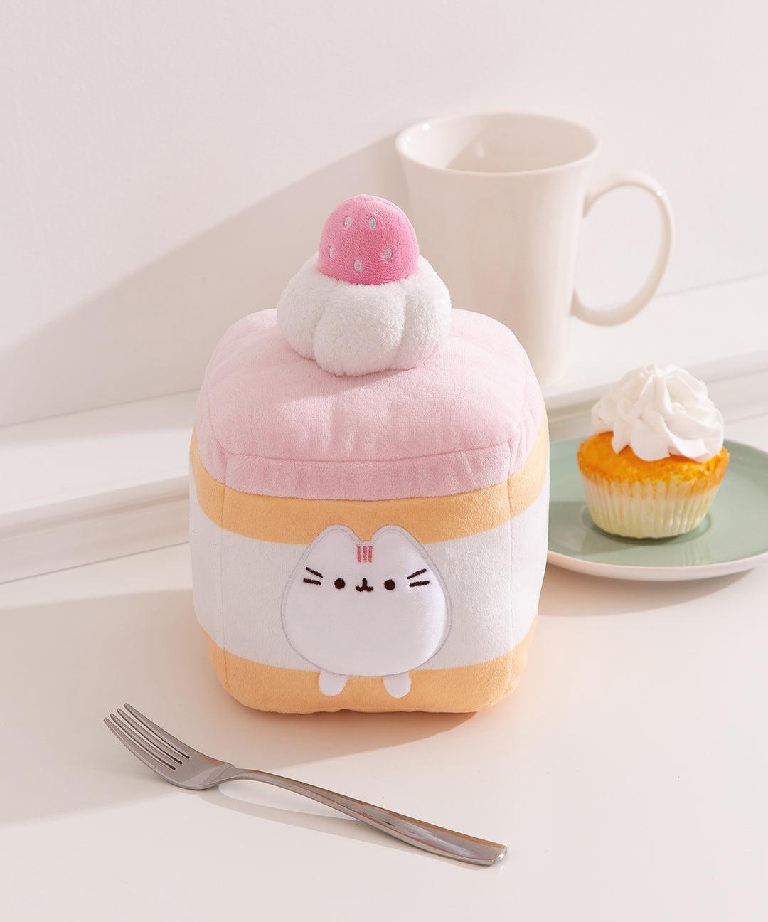 Front view of the Pusheen Sweets Strawberry Spongecake Squisheen Plush. The light yellow and pink Pusheen plush sits within the layers of the cake that's topped with whipped cream and a pink strawberry.
