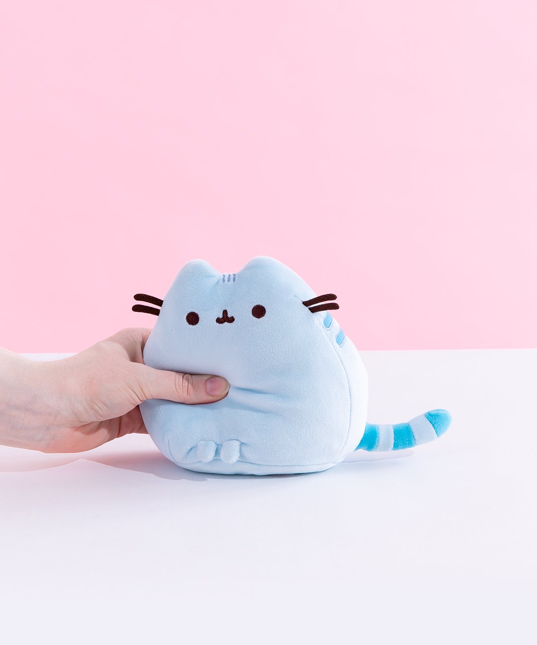 A model’s hand squeezing the Blue Mini Squisheen Plush, demonstrating it’s squishiness.