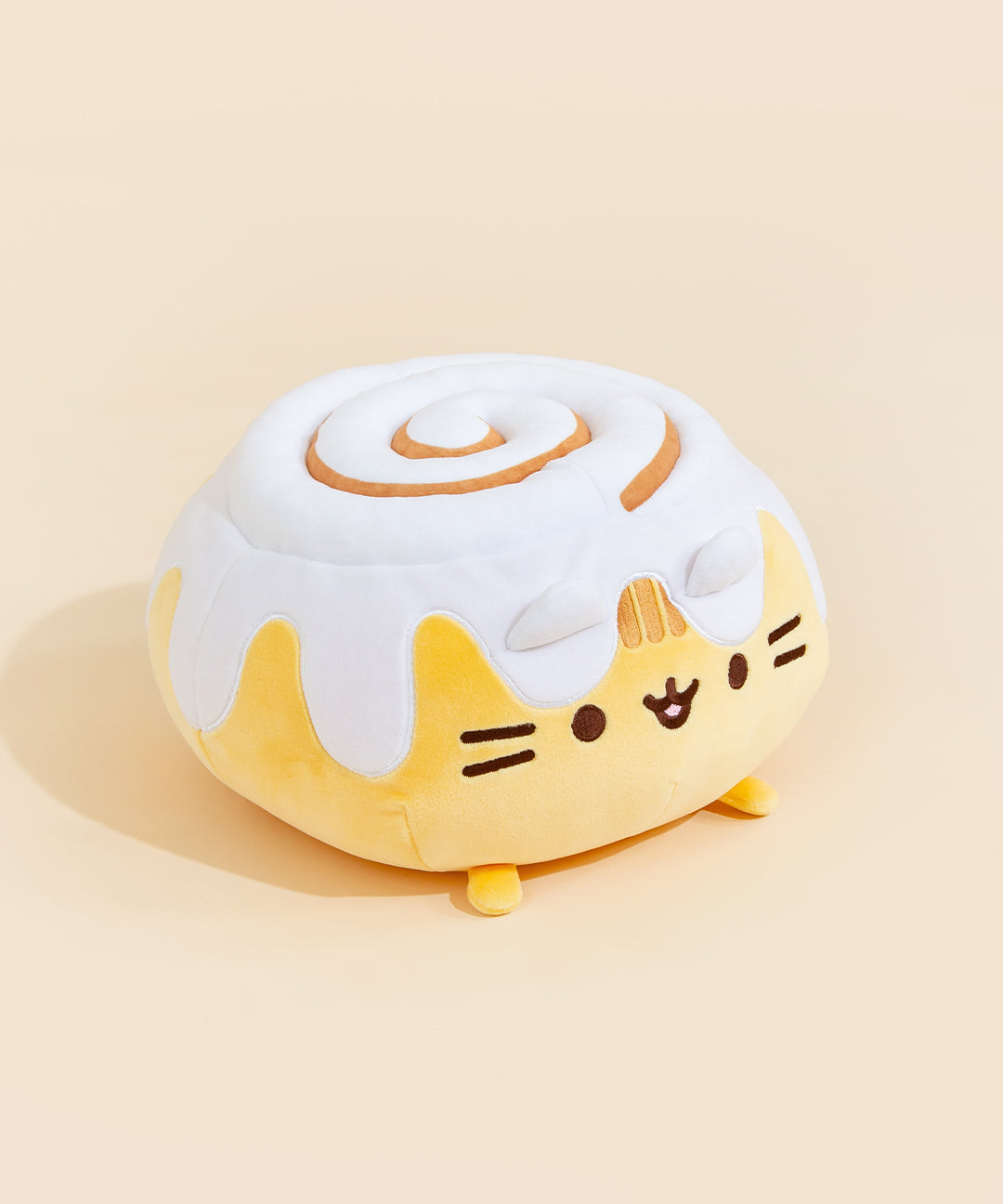 A quarter profile view of the Cinnamon Roll Squisheen, facing the right, in front of a cream background. The frosting on top of the cinnamon bun has an extra bit of plush filling.