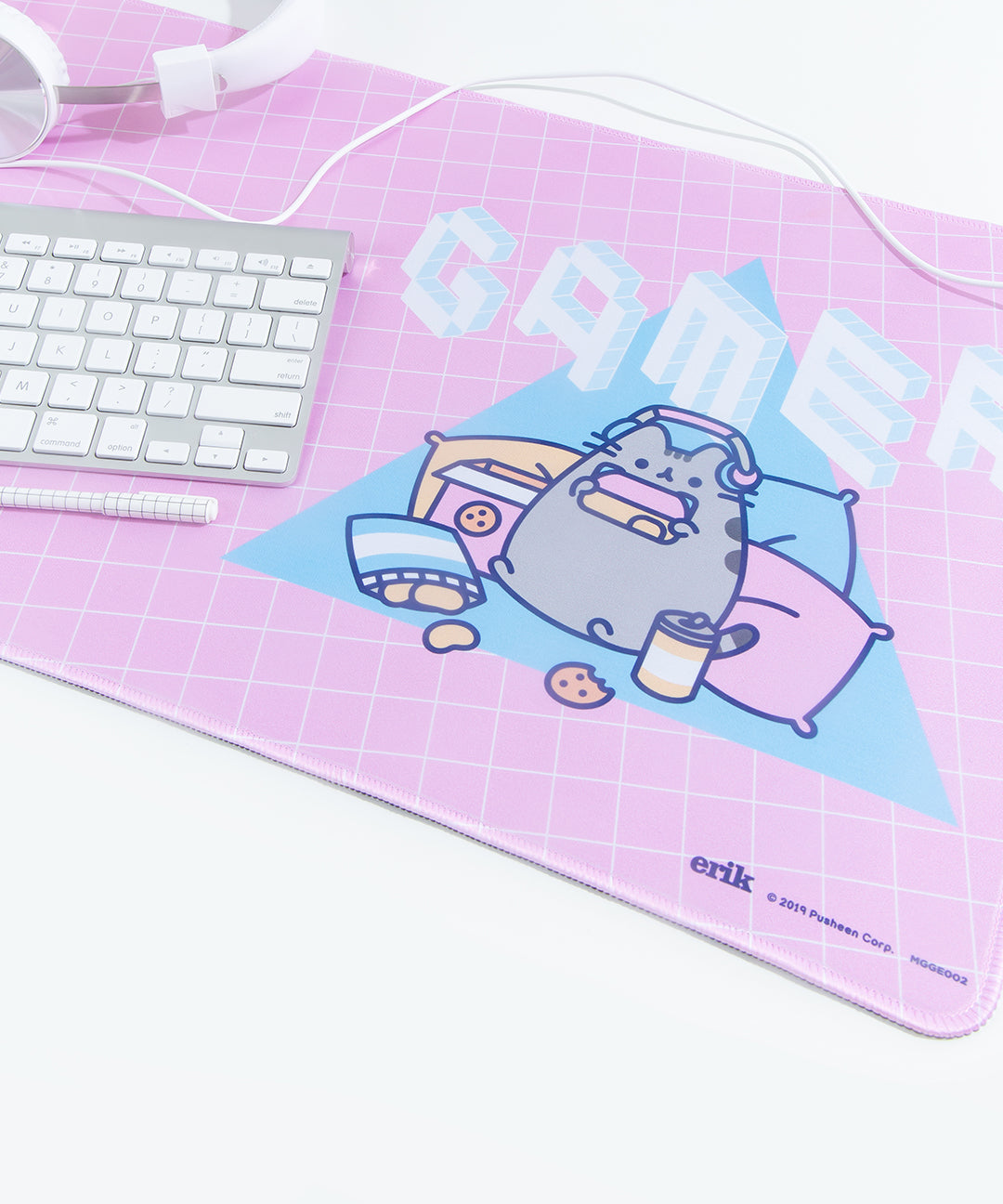 Angled close up of the Gamer Pusheen design on the Gaming Desk Mat. The white headphones, keyboard, and pen are partially visible, sitting on the left hand side of the mat. The Manufacturer details, copyright date and product number are visible on the lower right hand side of the mat.
