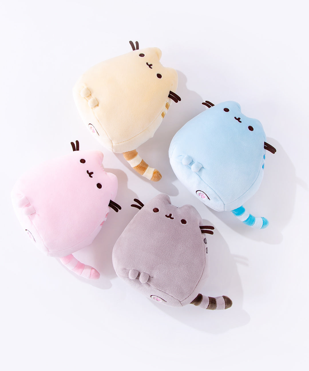 All four Mini Squisheen Plush laying on their backs on top of a white floor, the bottom of the plush partially visible. The flat bottom of the plush features two more feet and with pink paw prints embroidered into the plush.