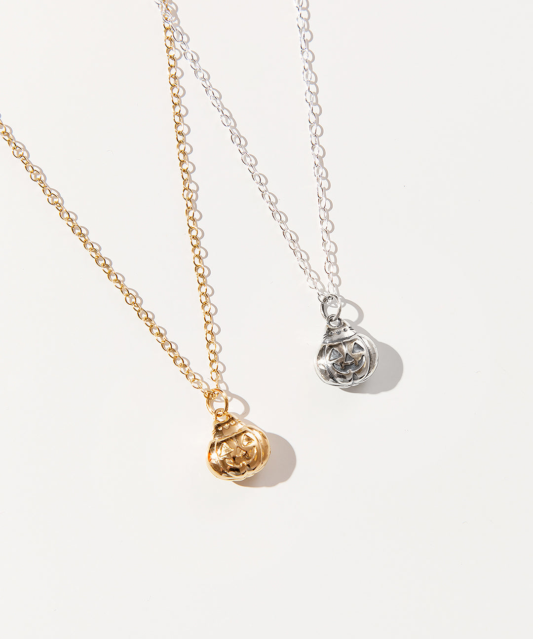 Gold and Silver charm necklaces next to one another. The charm features Pusheen sticking her head out of the top of a jack-o-lantern.
