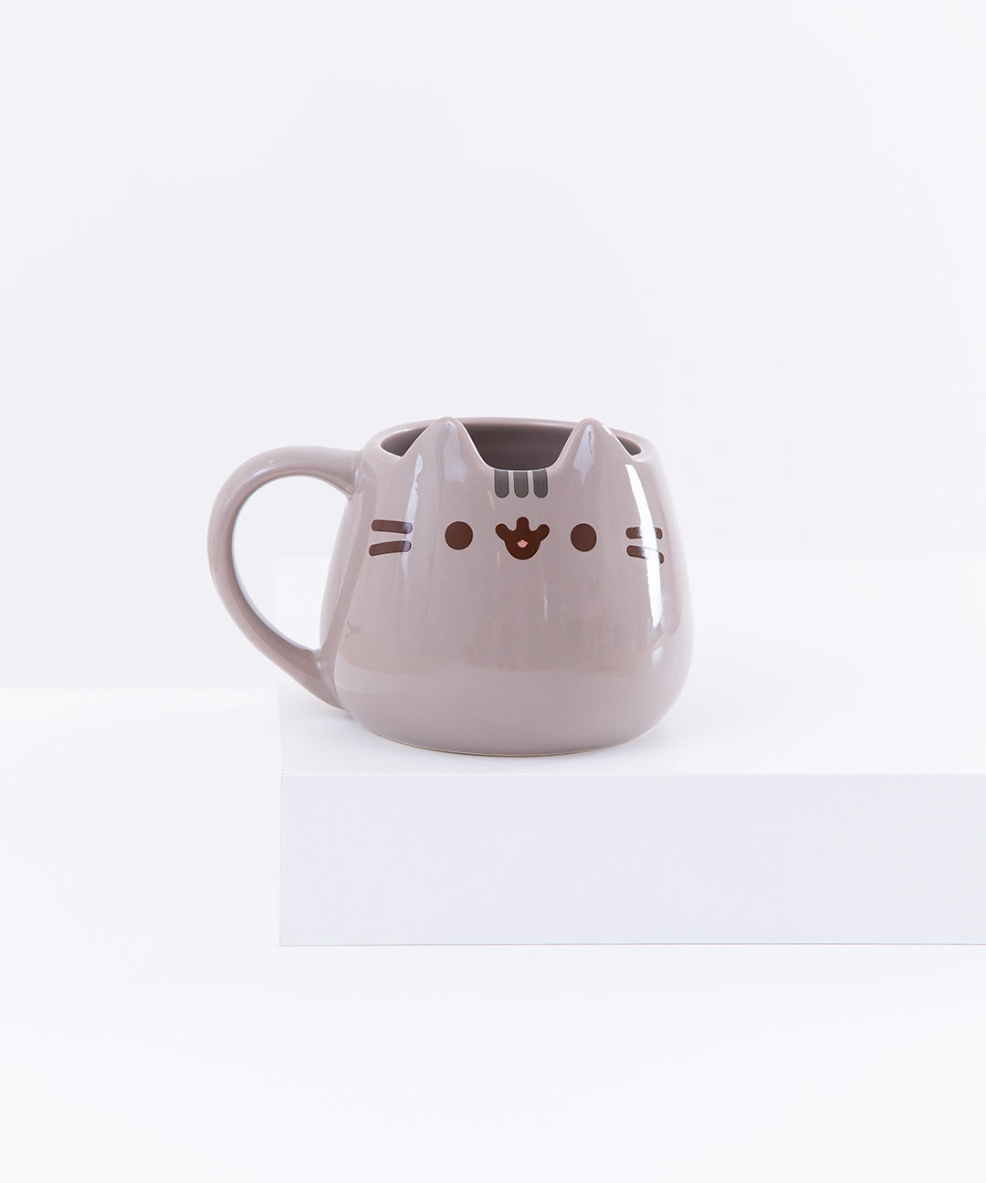 The Pusheen Character Mug resting on top of a white pedestal in front of a white background.