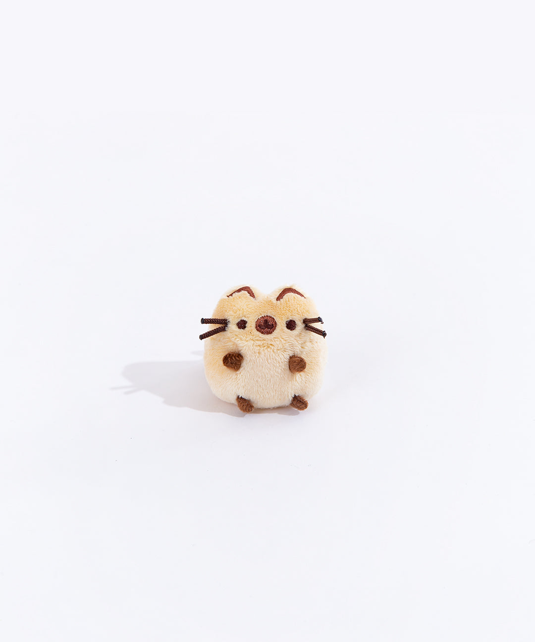 Full view of the mini Siamese cat plush from the collectors set. The cat is a light brown with dark brown paw stubs, a dark brown circle over their snout, and dark brown embroidered line on the top of their ears.