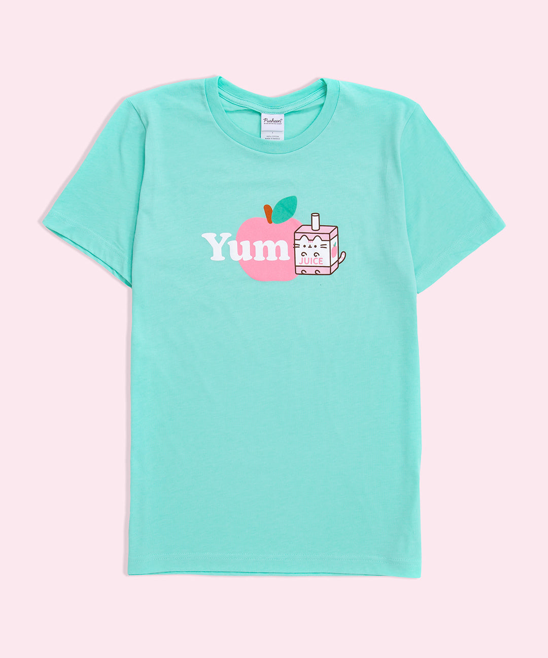 A mint green graphic tee against a light pink background. The graphic features Pusheen as Juice Box Sips next to the word ‘Yum’ in white, both in front of a pink apple. 